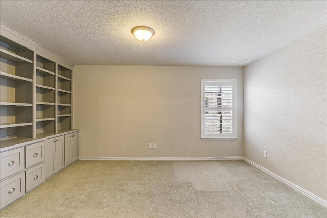 unfurnished room featuring light carpet, a textured ceiling, and baseboards