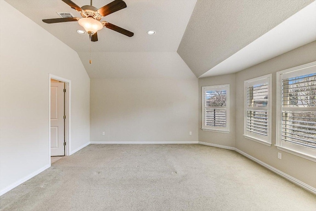 carpeted empty room with vaulted ceiling, a ceiling fan, baseboards, and visible vents