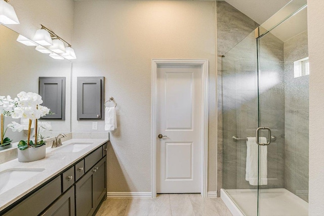 full bathroom with double vanity, a shower stall, baseboards, and a sink