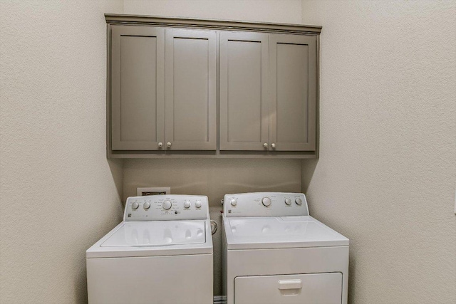 laundry area featuring cabinet space, washing machine and dryer, and a textured wall