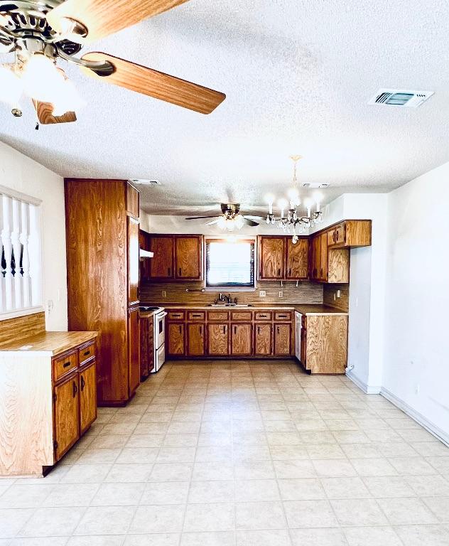 kitchen featuring visible vents, ceiling fan with notable chandelier, a sink, white electric stove, and brown cabinetry