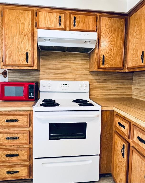 kitchen with under cabinet range hood, brown cabinets, white electric stove, and light countertops