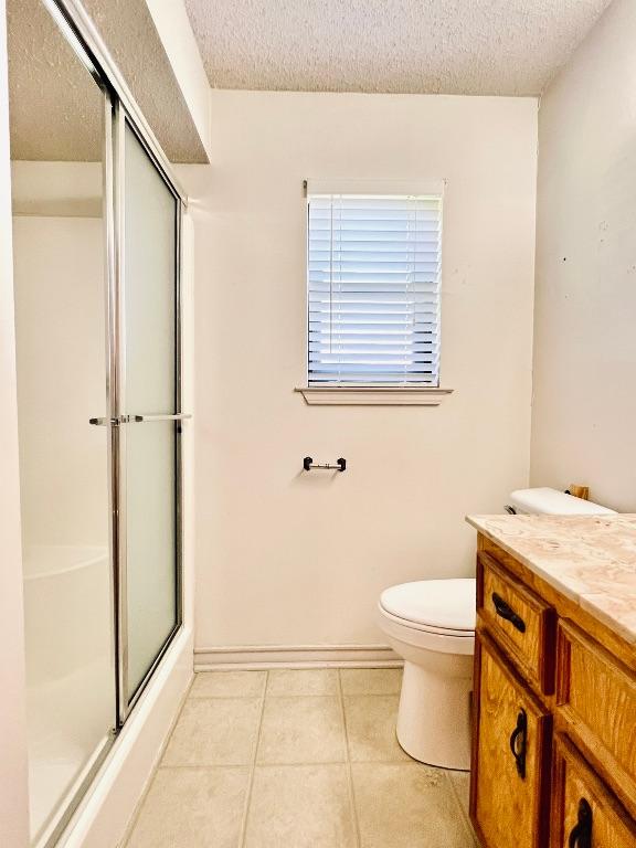 bathroom featuring toilet, vanity, tile patterned floors, an enclosed shower, and a textured ceiling