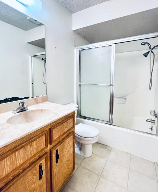 bathroom with tile patterned floors, toilet, a textured ceiling, shower / bath combination with glass door, and vanity