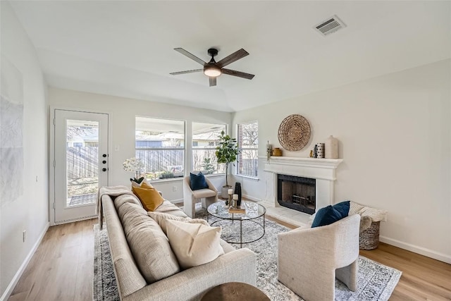 living area featuring visible vents, a fireplace with raised hearth, a ceiling fan, and light wood finished floors