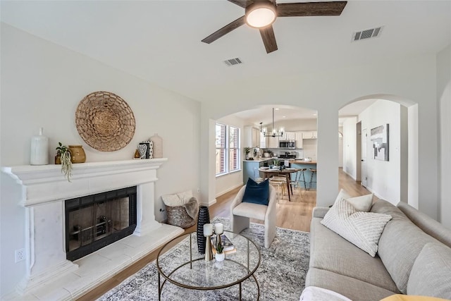 living room with arched walkways, visible vents, and ceiling fan with notable chandelier