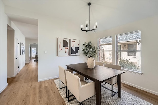 dining room with a notable chandelier, light wood-style floors, arched walkways, and baseboards