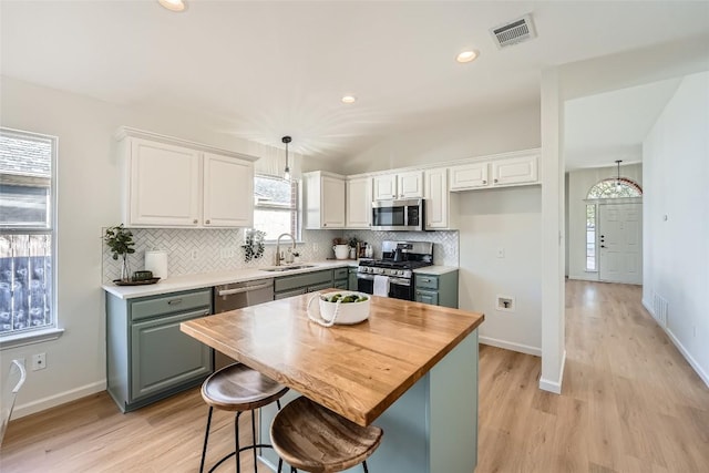 kitchen with visible vents, a sink, tasteful backsplash, stainless steel appliances, and light wood-style floors