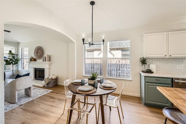 dining room featuring arched walkways, a fireplace with raised hearth, light wood-type flooring, and baseboards