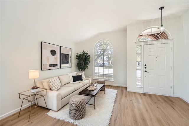 living room featuring lofted ceiling, light wood-style floors, and baseboards