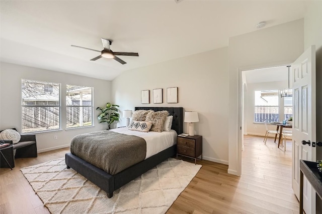 bedroom with ceiling fan with notable chandelier, vaulted ceiling, baseboards, and light wood-type flooring