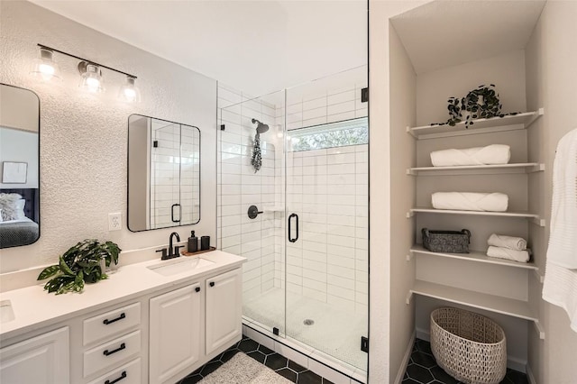 full bath with tile patterned flooring, a shower stall, double vanity, a textured wall, and a sink