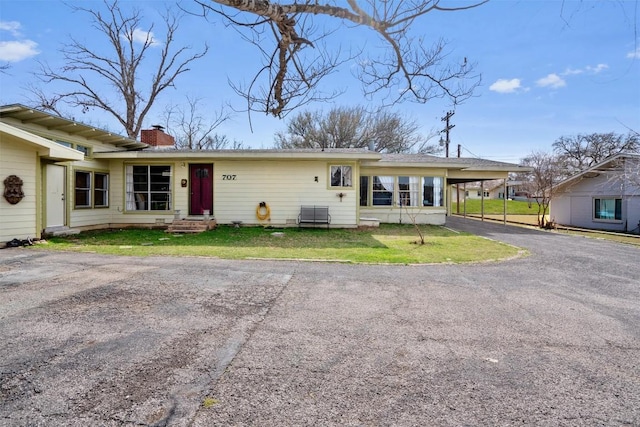 ranch-style home featuring aphalt driveway, a front lawn, a carport, and a chimney