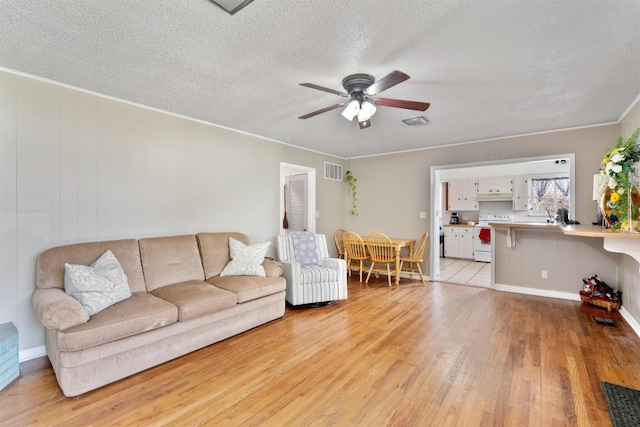 living room featuring light wood finished floors, visible vents, a textured ceiling, and a ceiling fan