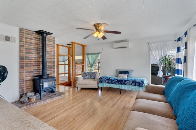 living area featuring a ceiling fan, wood finished floors, visible vents, a wall mounted AC, and a wood stove