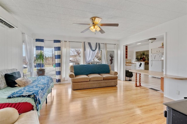 living room featuring ceiling fan, a wall mounted air conditioner, visible vents, and light wood-style flooring