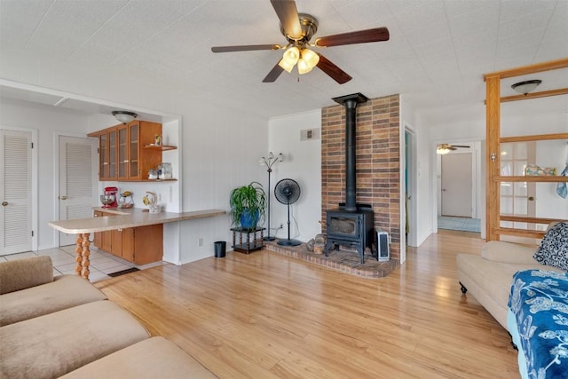 living room featuring a wood stove, light wood-style floors, visible vents, and ceiling fan