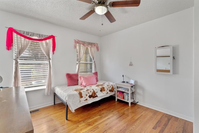 bedroom featuring visible vents, a textured ceiling, baseboards, and wood finished floors