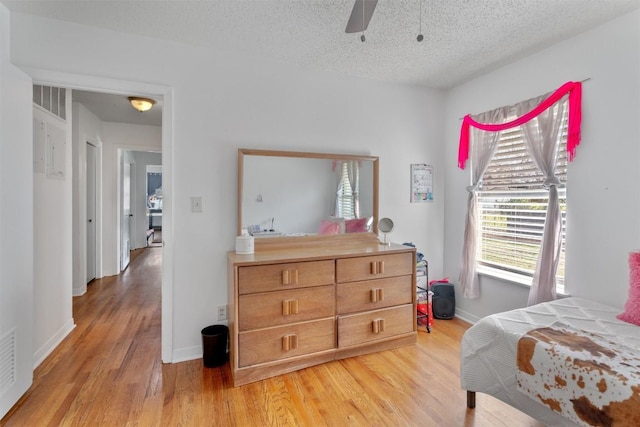 bedroom with a ceiling fan, light wood-style floors, baseboards, and a textured ceiling