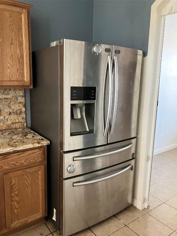 kitchen featuring tasteful backsplash, light tile patterned flooring, stainless steel fridge, and brown cabinets