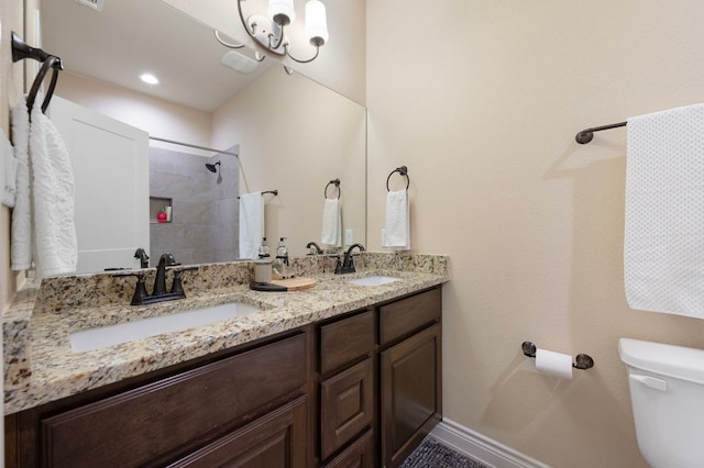 full bathroom featuring a sink, tiled shower, toilet, and double vanity