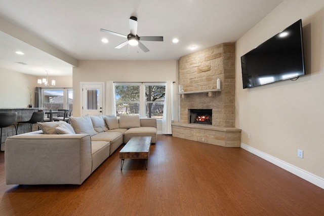 living room featuring baseboards, recessed lighting, ceiling fan with notable chandelier, a fireplace, and wood finished floors