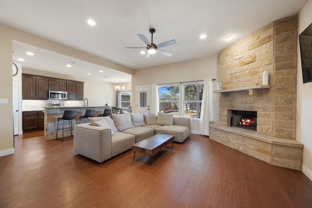 living area featuring baseboards, a stone fireplace, recessed lighting, ceiling fan with notable chandelier, and wood finished floors