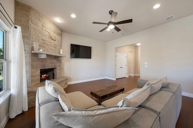 living area featuring visible vents, a ceiling fan, a stone fireplace, baseboards, and dark wood-style flooring