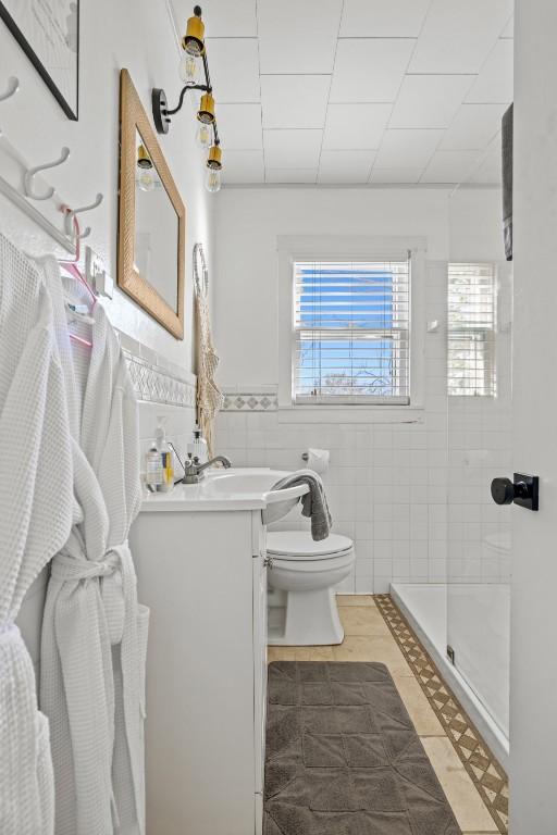 full bathroom featuring toilet, a stall shower, tile walls, wainscoting, and vanity