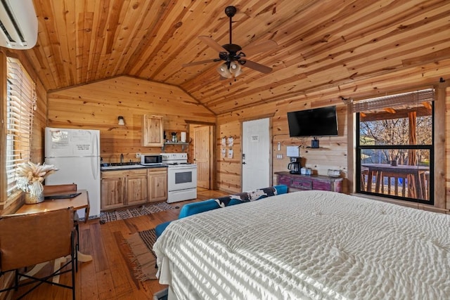 bedroom featuring an AC wall unit, a sink, hardwood / wood-style floors, freestanding refrigerator, and vaulted ceiling