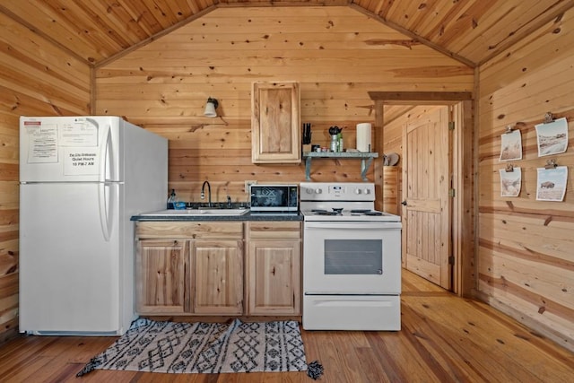 kitchen featuring light wood-style flooring, a sink, white appliances, wood walls, and lofted ceiling