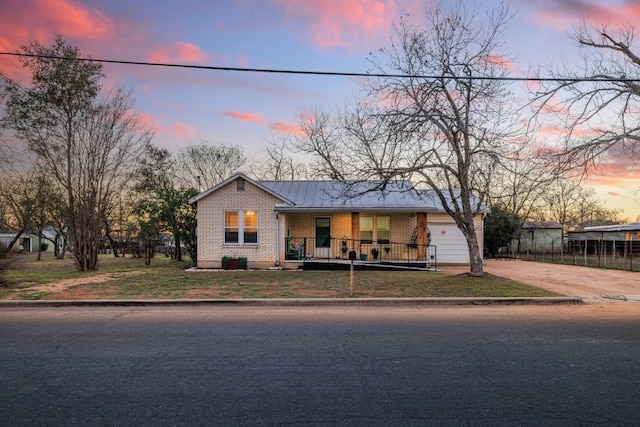 view of front facade with brick siding, a porch, a lawn, metal roof, and a standing seam roof