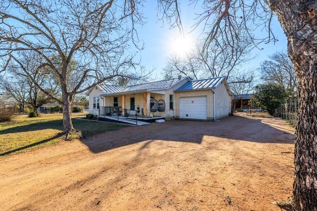 view of front facade featuring dirt driveway, a porch, a front yard, a garage, and a standing seam roof