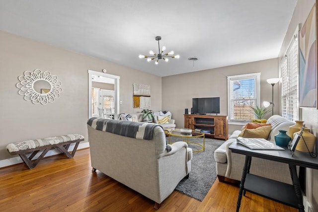 living room featuring a chandelier, baseboards, visible vents, and wood finished floors