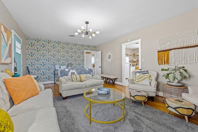 living area featuring wallpapered walls, an accent wall, baseboards, a chandelier, and wood finished floors