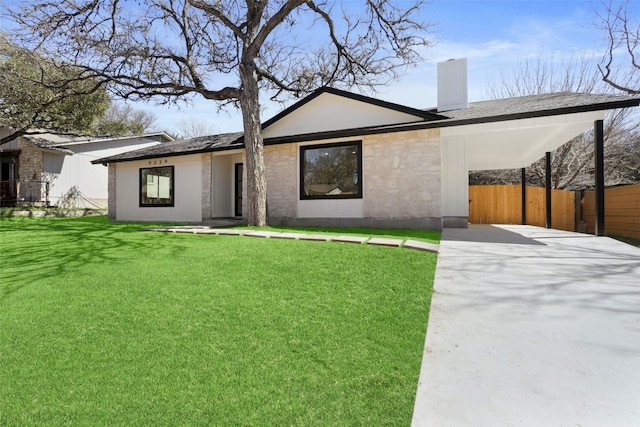 view of front facade with a front yard, fence, a chimney, a carport, and concrete driveway