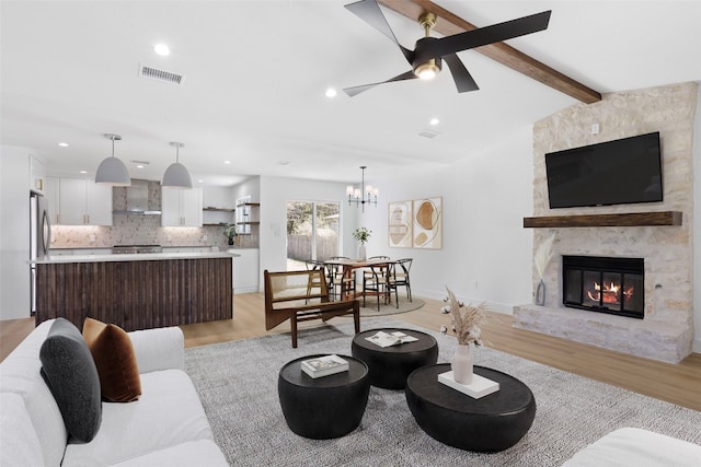 living room with visible vents, light wood-style flooring, ceiling fan with notable chandelier, a stone fireplace, and vaulted ceiling with beams