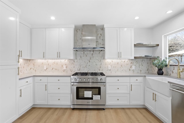 kitchen with a sink, light countertops, white cabinets, appliances with stainless steel finishes, and wall chimney range hood