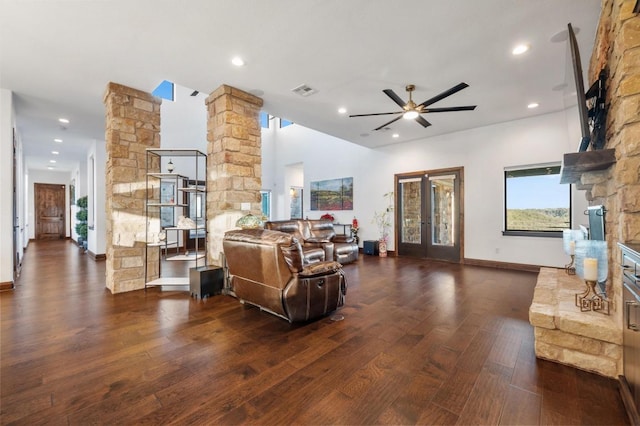 living room with dark wood finished floors, ornate columns, a stone fireplace, recessed lighting, and a ceiling fan