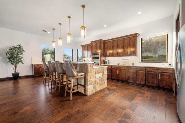 kitchen featuring a kitchen island, dark wood finished floors, light countertops, appliances with stainless steel finishes, and a kitchen breakfast bar