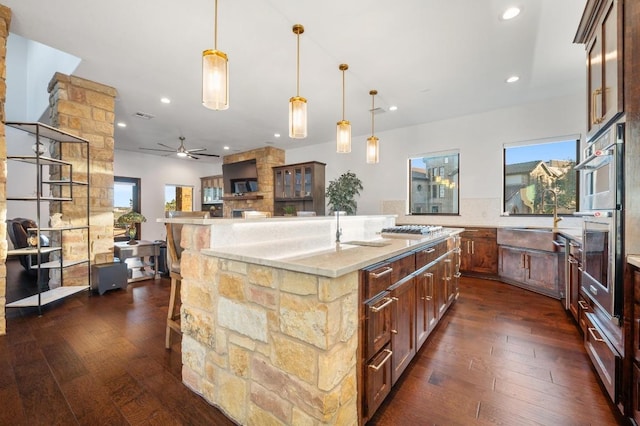 kitchen featuring light stone counters, a spacious island, dark wood-style flooring, a sink, and open floor plan