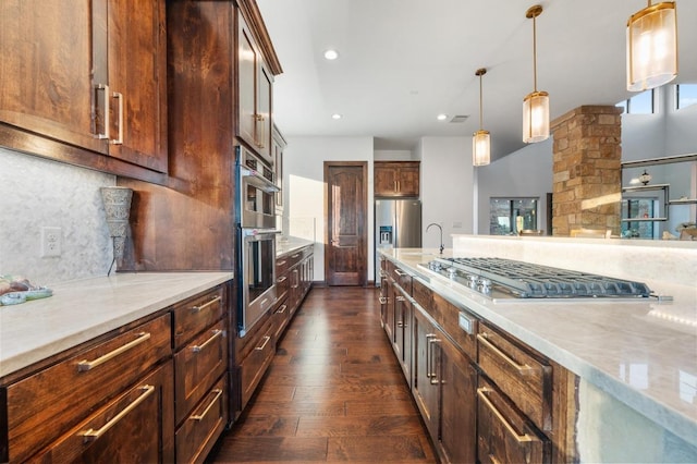 kitchen with pendant lighting, light stone counters, backsplash, dark wood finished floors, and stainless steel appliances