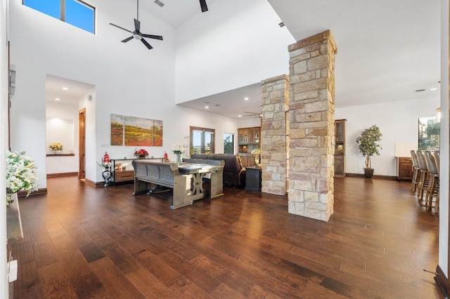 living room featuring dark wood-type flooring, decorative columns, baseboards, and ceiling fan