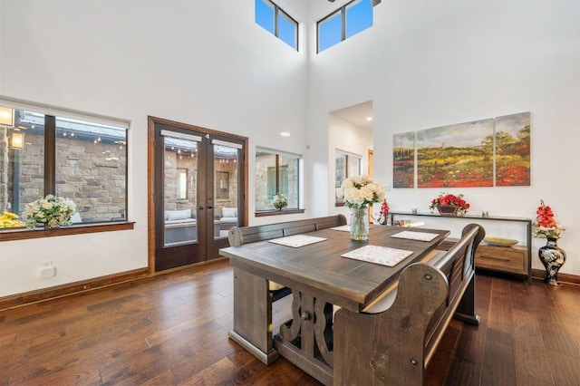 dining room featuring a towering ceiling, wood finished floors, baseboards, and french doors