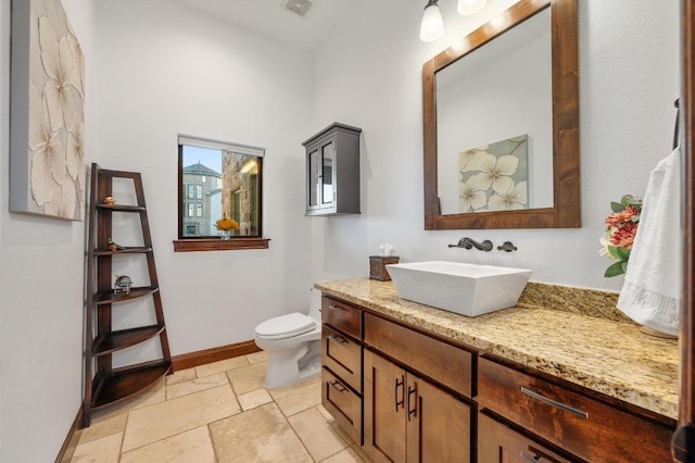 bathroom with visible vents, baseboards, toilet, stone tile floors, and vanity