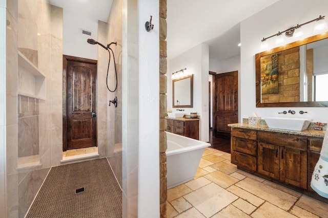 full bathroom featuring a tile shower, a freestanding bath, vanity, and stone tile flooring