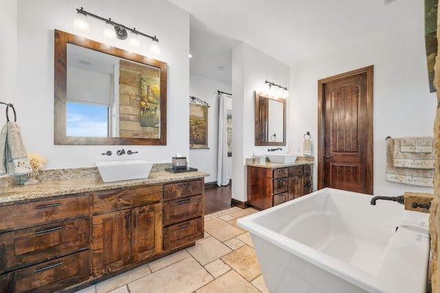 full bath featuring a freestanding tub, two vanities, and a sink