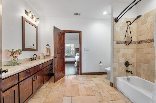 ensuite bathroom with visible vents, connected bathroom, toilet, stone tile flooring, and vanity