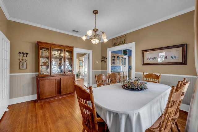 dining area with visible vents, a wainscoted wall, light wood finished floors, ornamental molding, and a chandelier