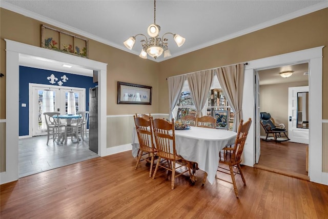 dining area featuring wood finished floors, a wainscoted wall, french doors, crown molding, and a notable chandelier